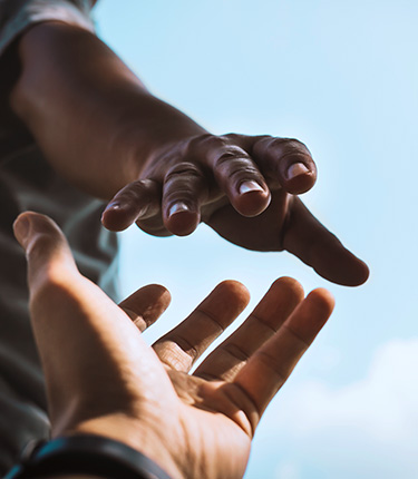 Two hands extending toward one another against blue sky.