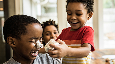 Toddler smushes cupcake on brothers nose.