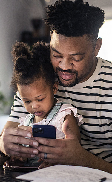 Father using mobile device with his daughter sitting on his lap.