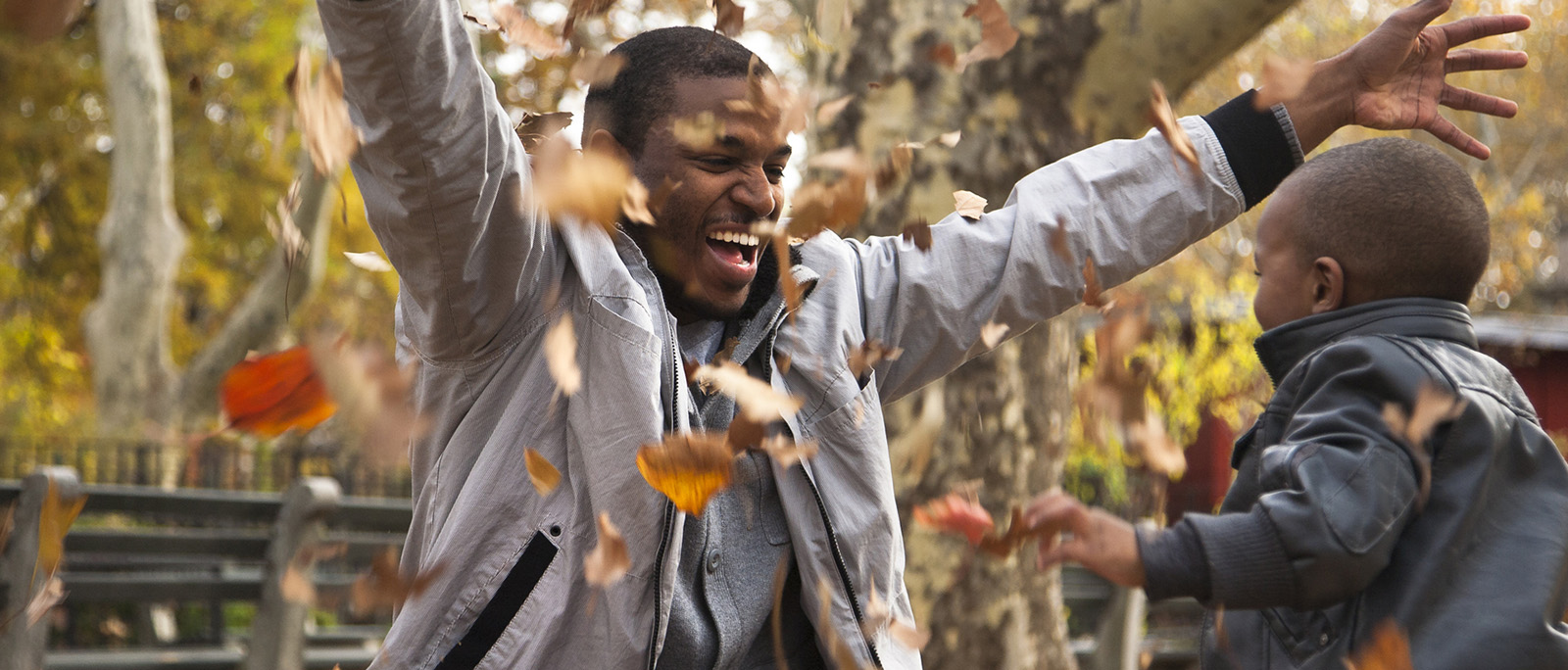 A man and a boy play with fall leaves, throwing them above and around them.