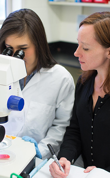 Teacher interacting with a student utilizing a microscope.