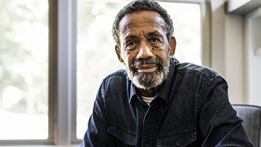 A man framed by sunny windows smiles toward the camera.