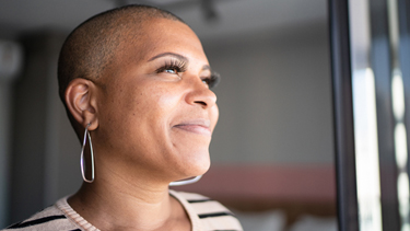 Bald woman looks confidently out window. 